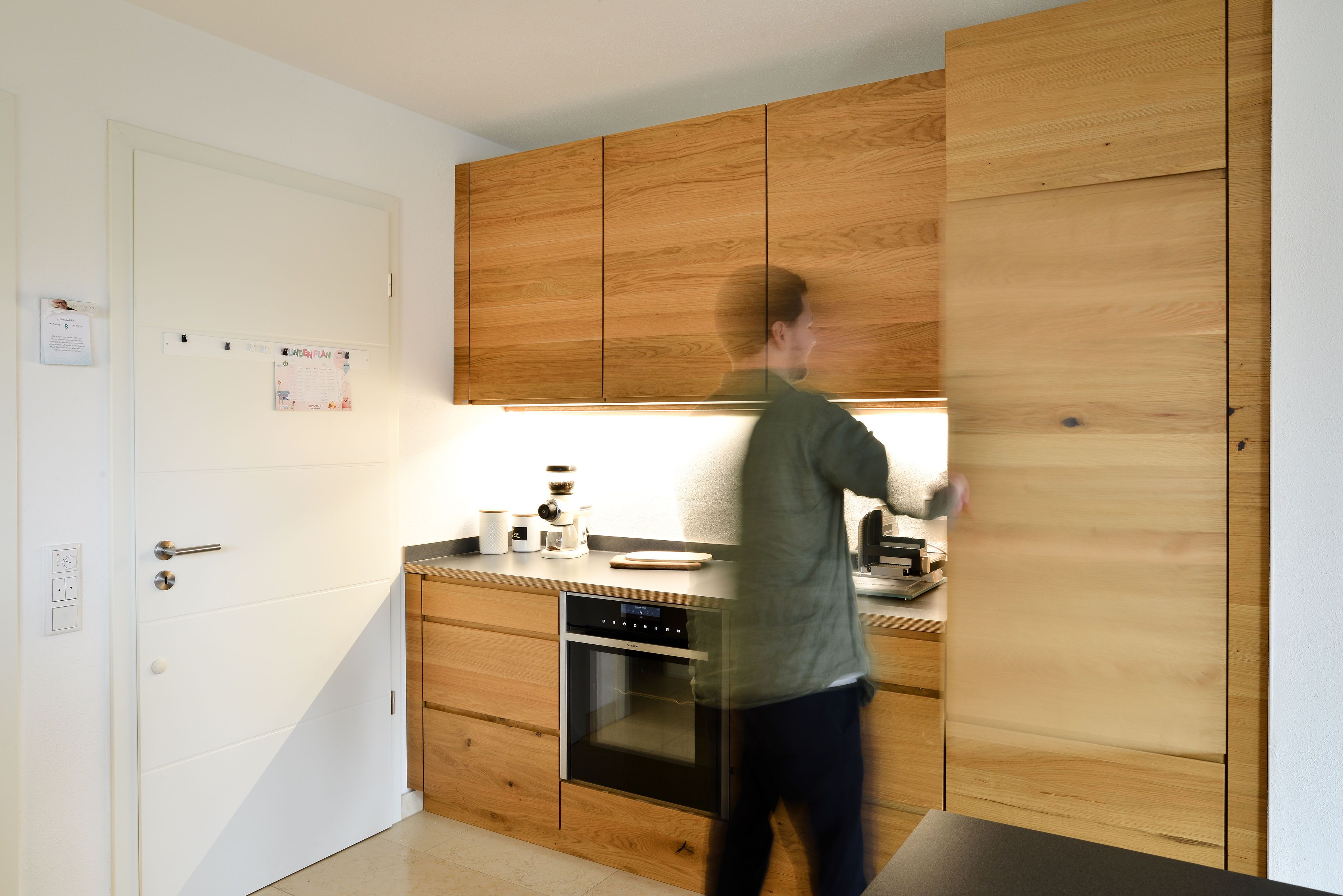 Moderne Einbauküche von Nuance Living mit Fronten in Eiche-Optik, integrierter Beleuchtung und hochwertigem Backofen.