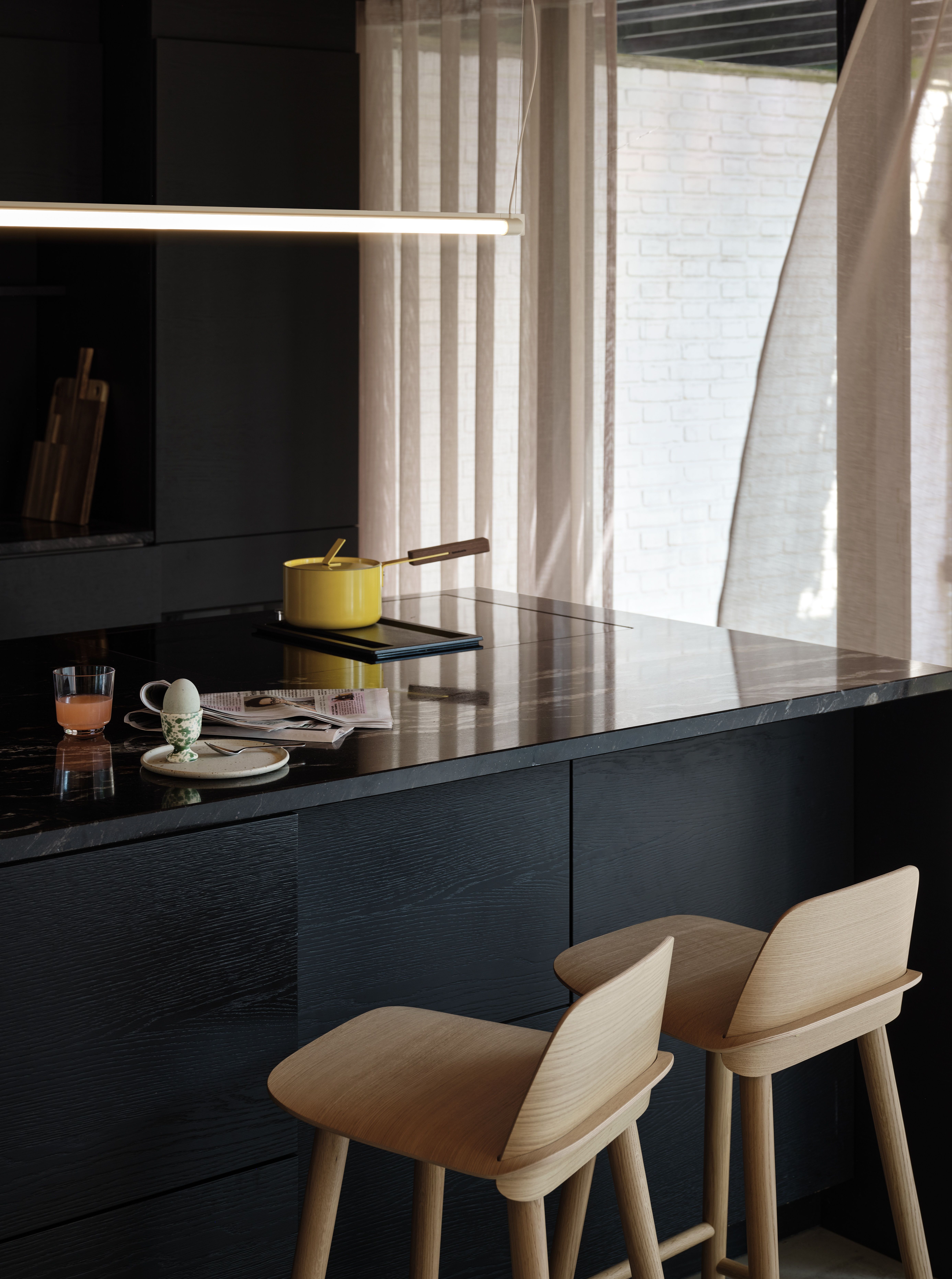 Kücheninsel mit schwarzer Marmorarbeitsplatte, Induktionskochfeld und Barhockern aus Eiche.