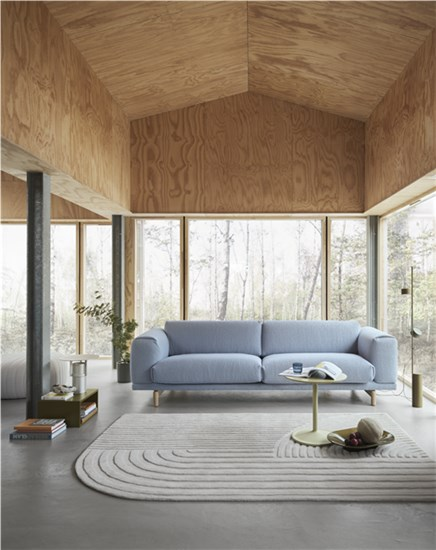 Helles Wohnzimmer mit Holzdecke, einem modernen hellblauen Sofa und einem strukturierten Teppich vor großen Fenstern