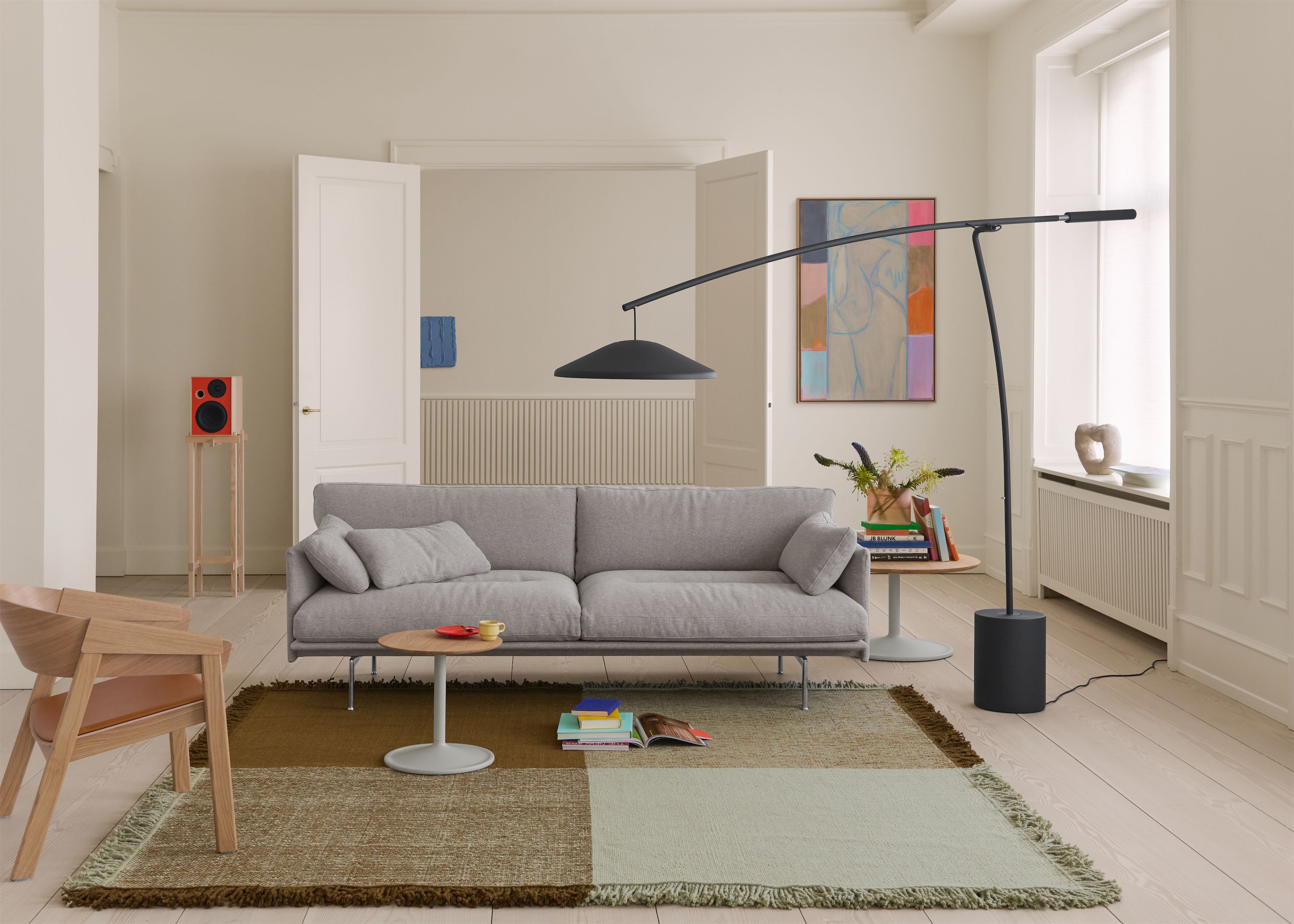 Helles Wohnzimmer mit grauem Sofa, Bogenstehleuchte und farbigem Teppich vor großen Altbaufenstern.